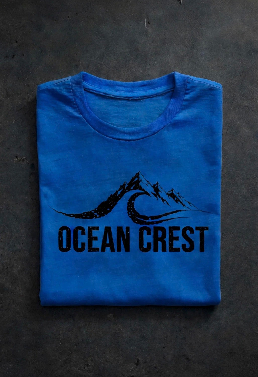 Folded blue t-shirt with black OCEAN CREST graphic on front.