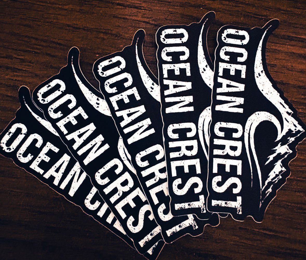 Five OCEAN CREST die-cut stickers fanned on dark wood.