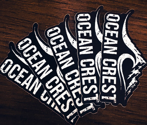 Five OCEAN CREST die-cut stickers fanned on dark wood.